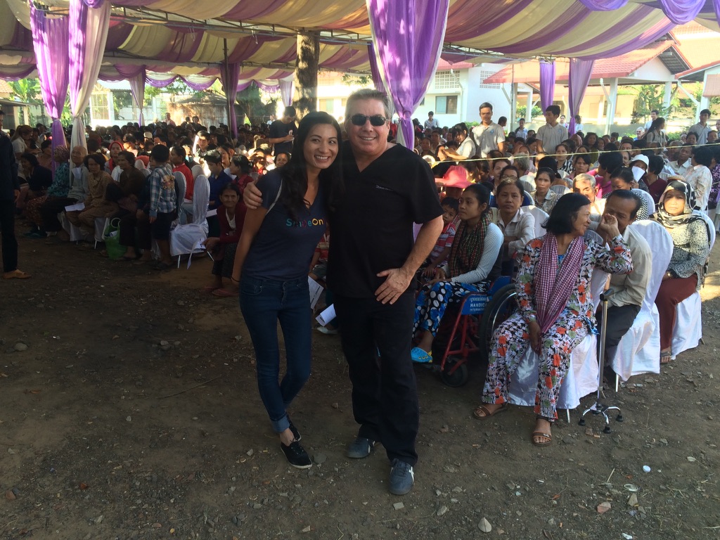 Steve Bender and a volunteer stand in front of hundreds of patients seated under a large tent, waiting to be seen at the clinic