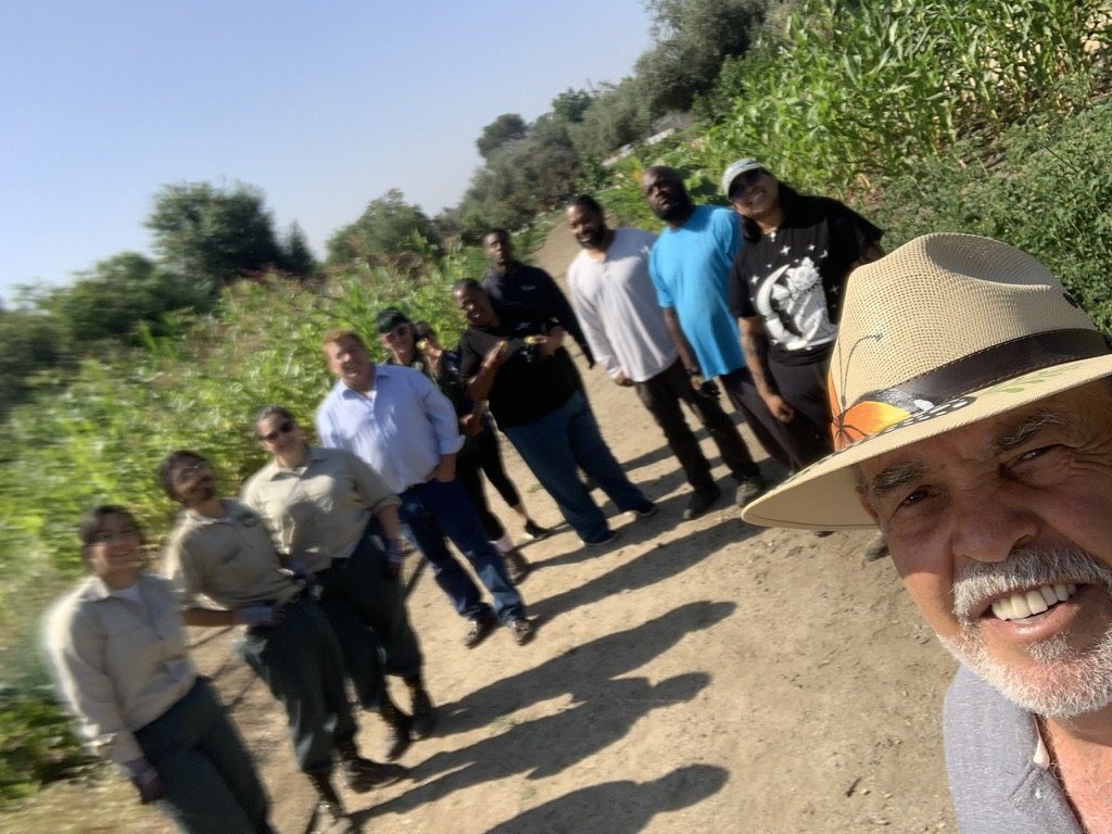A line of volunteers on a garden path beside tall corn, photographed in a selfie